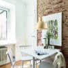 Cómoda mesa de comedor blanca en interiores con pared de ladrillo visto, estilo moderno y decoración minimalista.