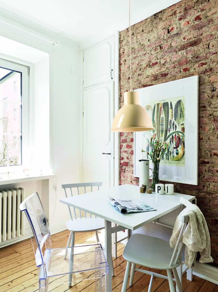 Cómoda mesa de comedor blanca en interiores con pared de ladrillo visto, estilo moderno y decoración minimalista.